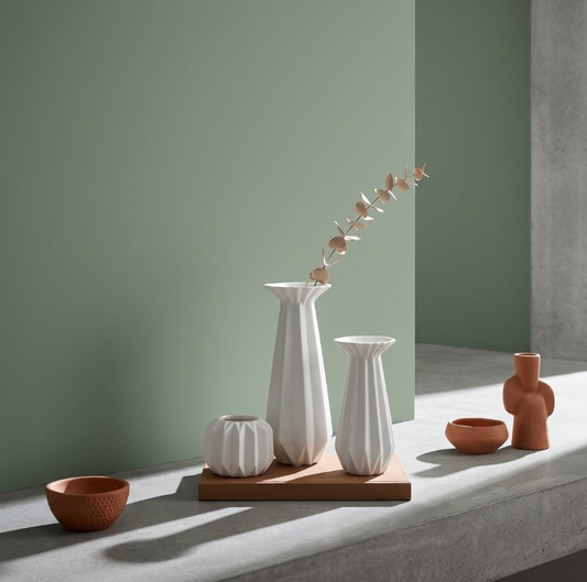 Sculptural white ribbed porcelain candle holders styled with a dried eucalyptus stem and terracotta accents against a sage green wall