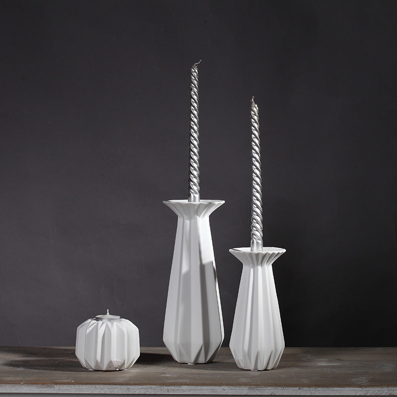 Three white faceted porcelain candlestick holders with tall twisted candles and a small tealight holder on a dark background