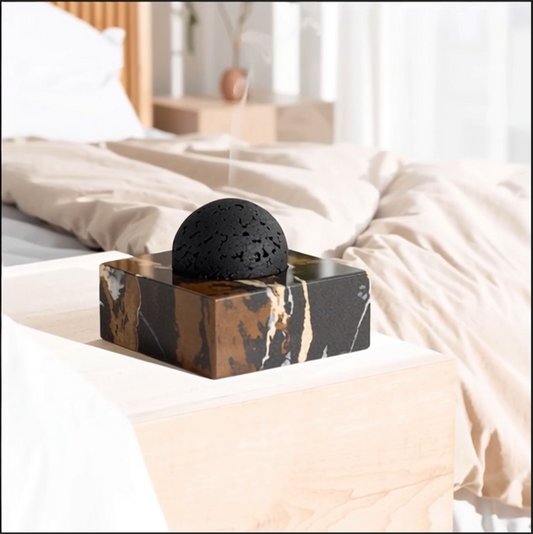 Marble and travertine ritual diffuser with black volcanic stone on a styled bed