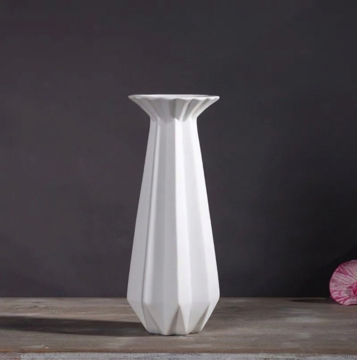 Tall white faceted porcelain candlestick holder with a flared rim on a dark gray background