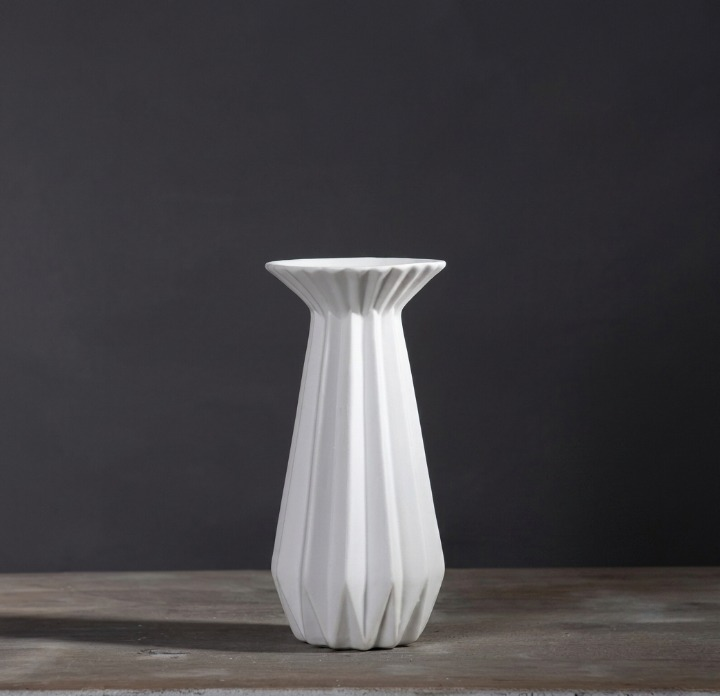 Medium white faceted porcelain candle holder with a flared opening on a dark gray background