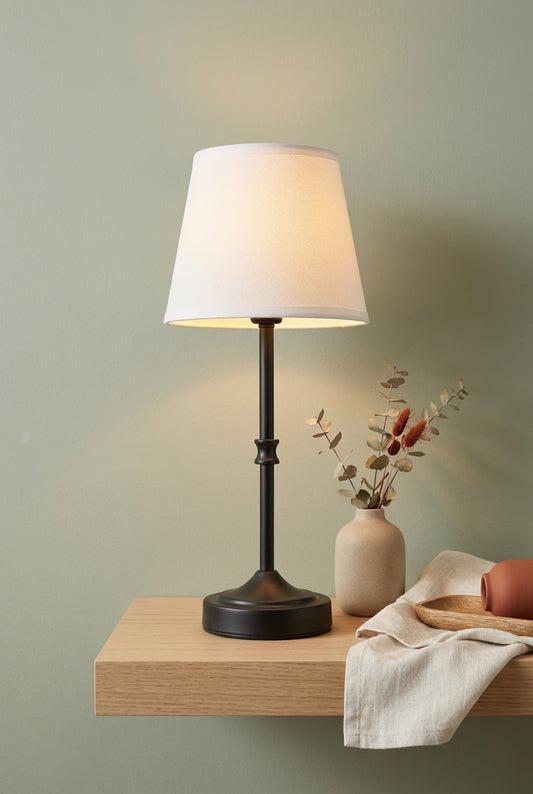 Black cordless table lamp glowing on an oak shelf against a sage-green wall with dried eucalyptus