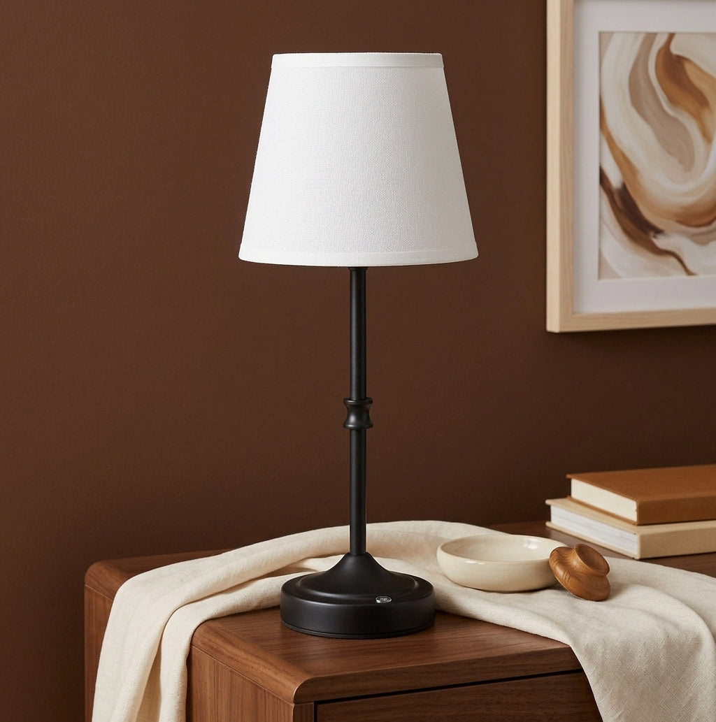 Rechargeable black table lamp with white shade on a walnut nightstand against a warm brown wall