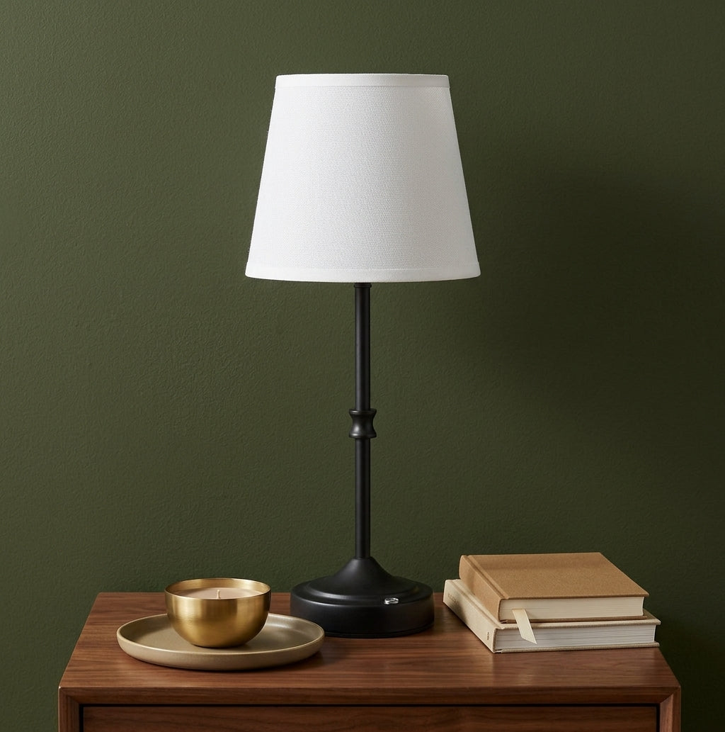 Cordless table lamp on a walnut nightstand against an olive-green wall with books and a brass candle