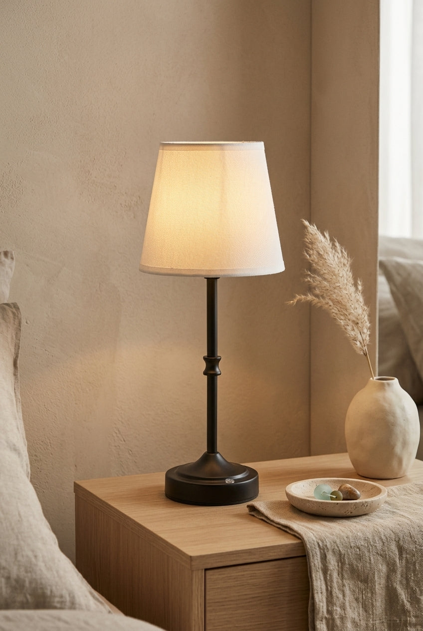 Rechargeable table lamp lit on a wood nightstand in a warm Japandi bedroom with pampas grass
