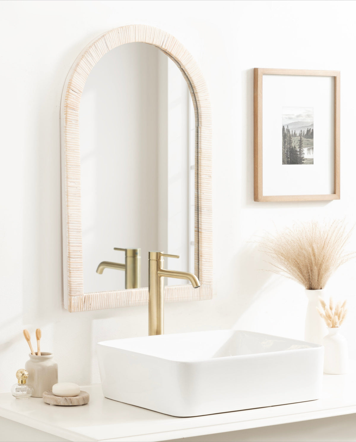 White rattan arched mirror above a vanity with a gold faucet