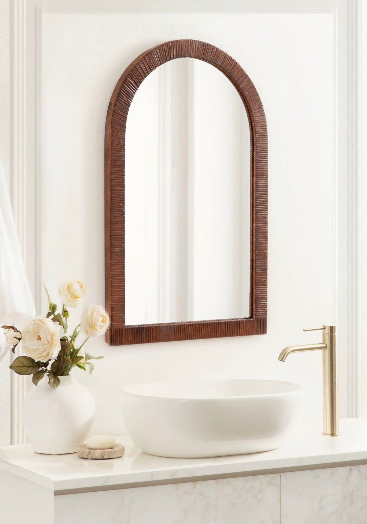 Brown rattan arched mirror above a vanity with white roses