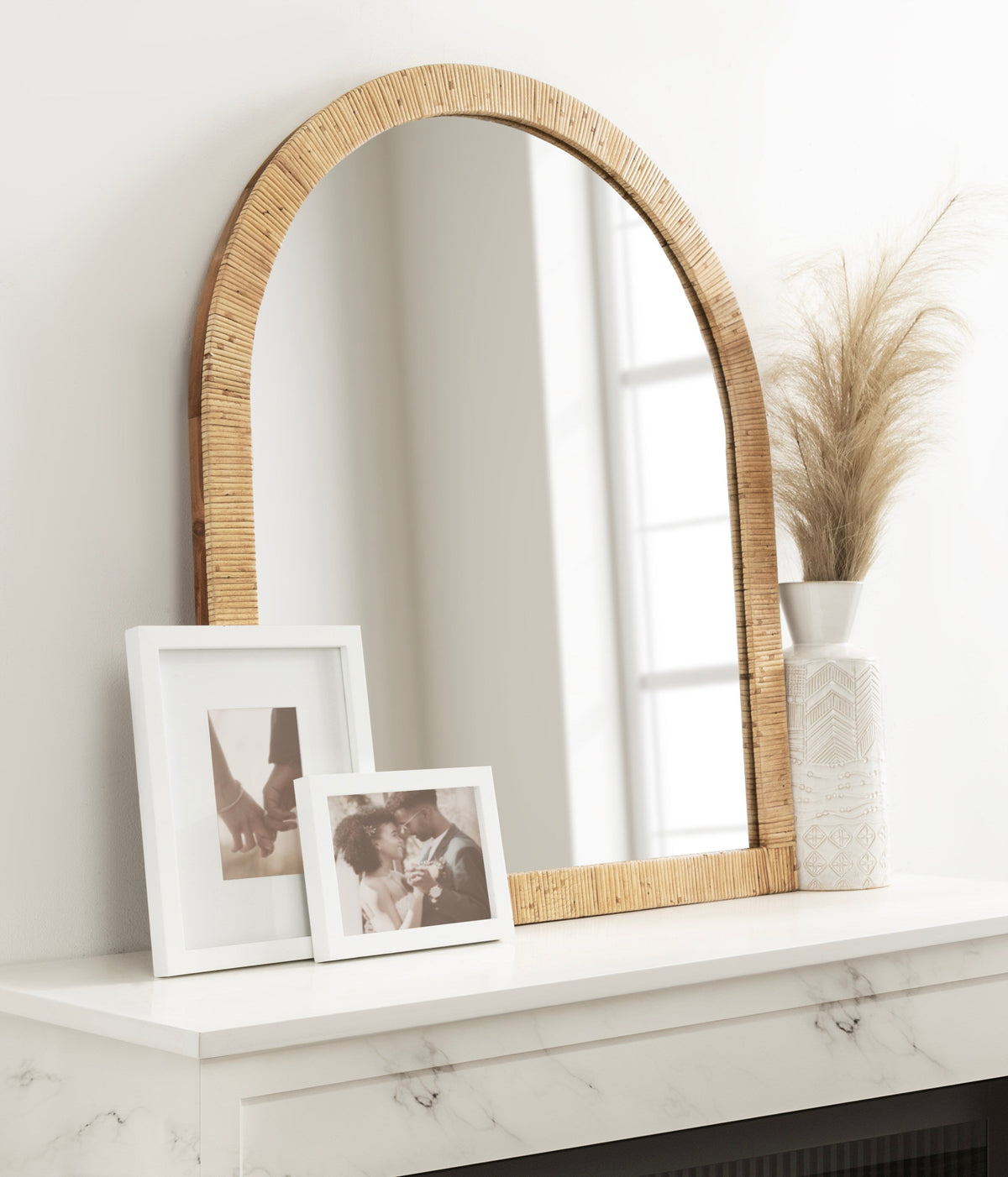 Natural rattan arched mirror on a mantel with framed photos