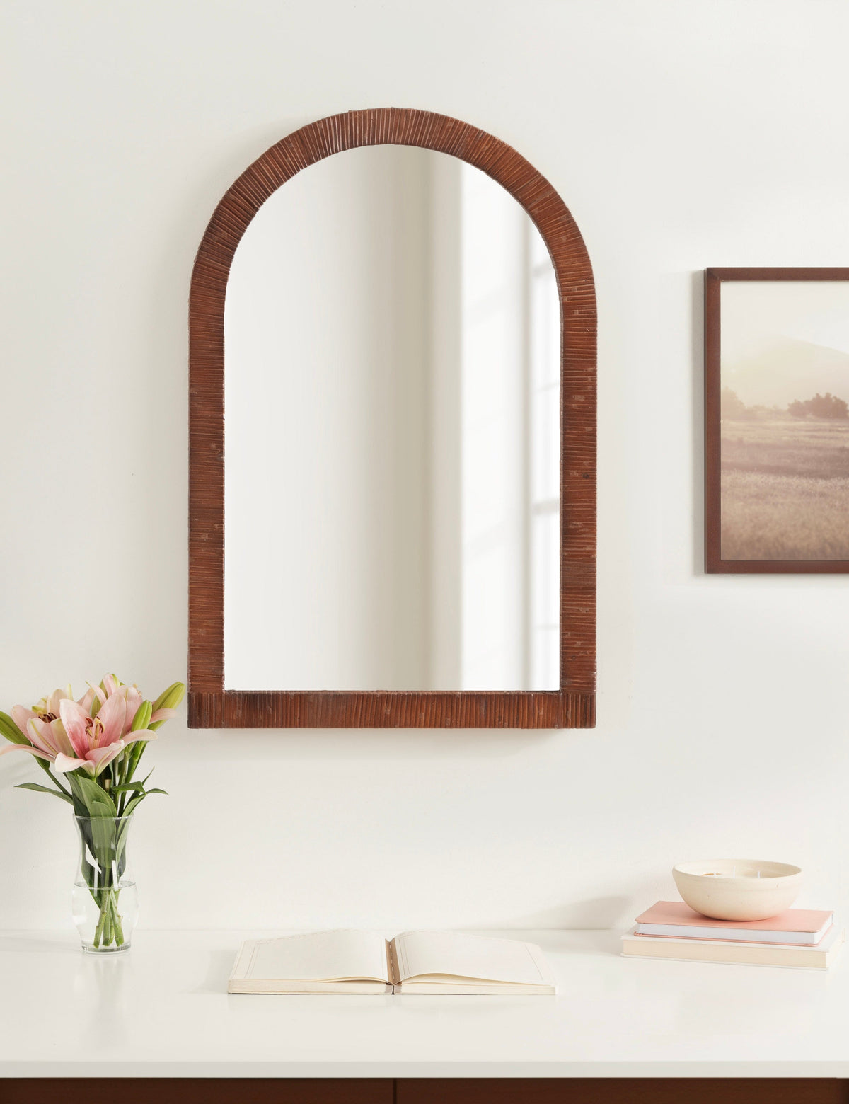 Brown rattan arched mirror above a console with pink tulips