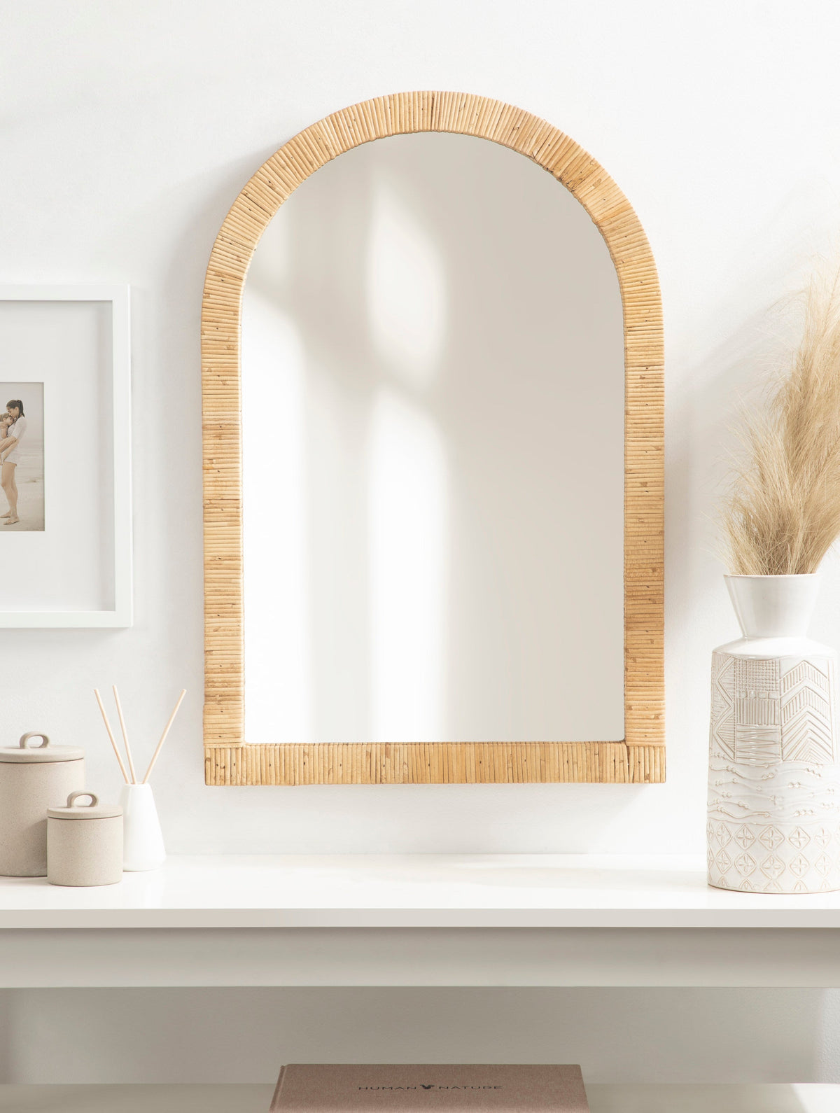 Natural rattan arched mirror above a vanity with white ceramic decor