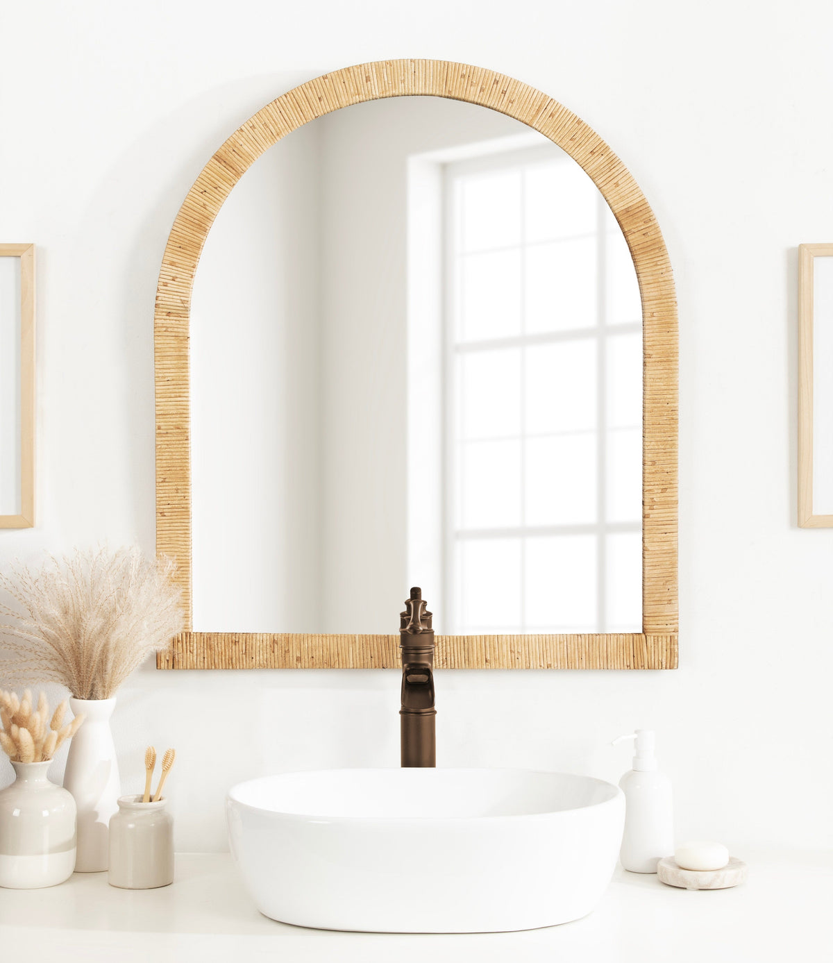 Natural rattan arched wall mirror above a bathroom vessel sink with pampas grass