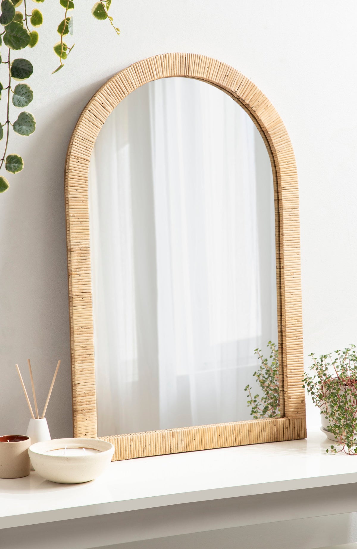Natural rattan arched mirror on a shelf with a trailing plant
