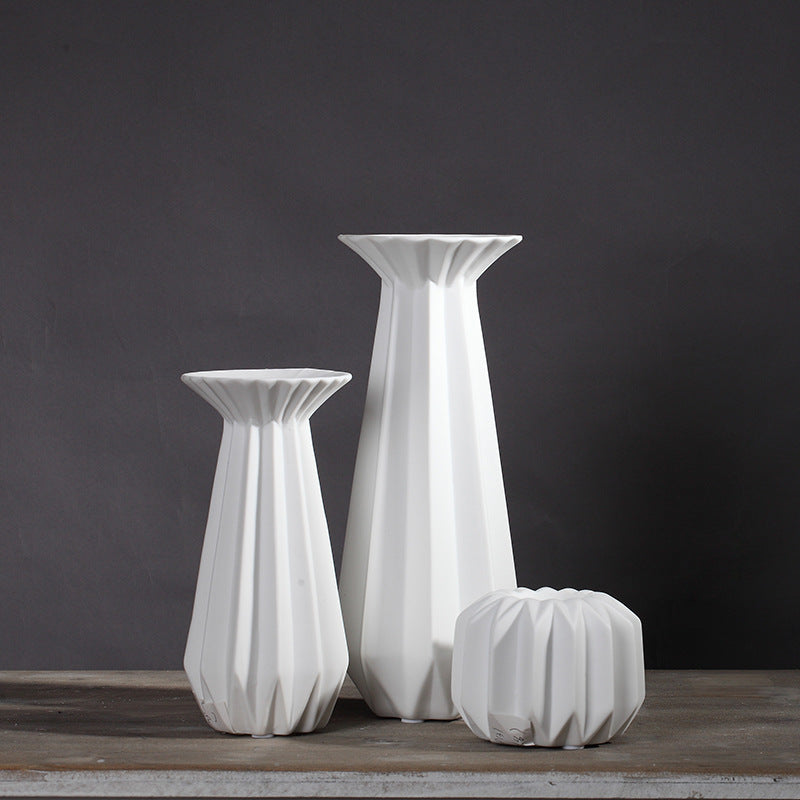Set of three sculptural white faceted porcelain candle holders in graduated sizes on a dark gray background