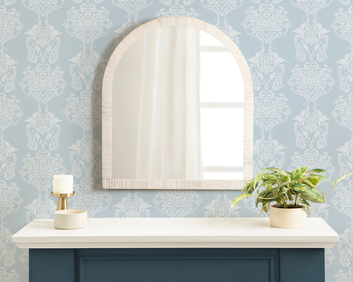 White rattan arched mirror on a blue-wallpapered wall above a console
