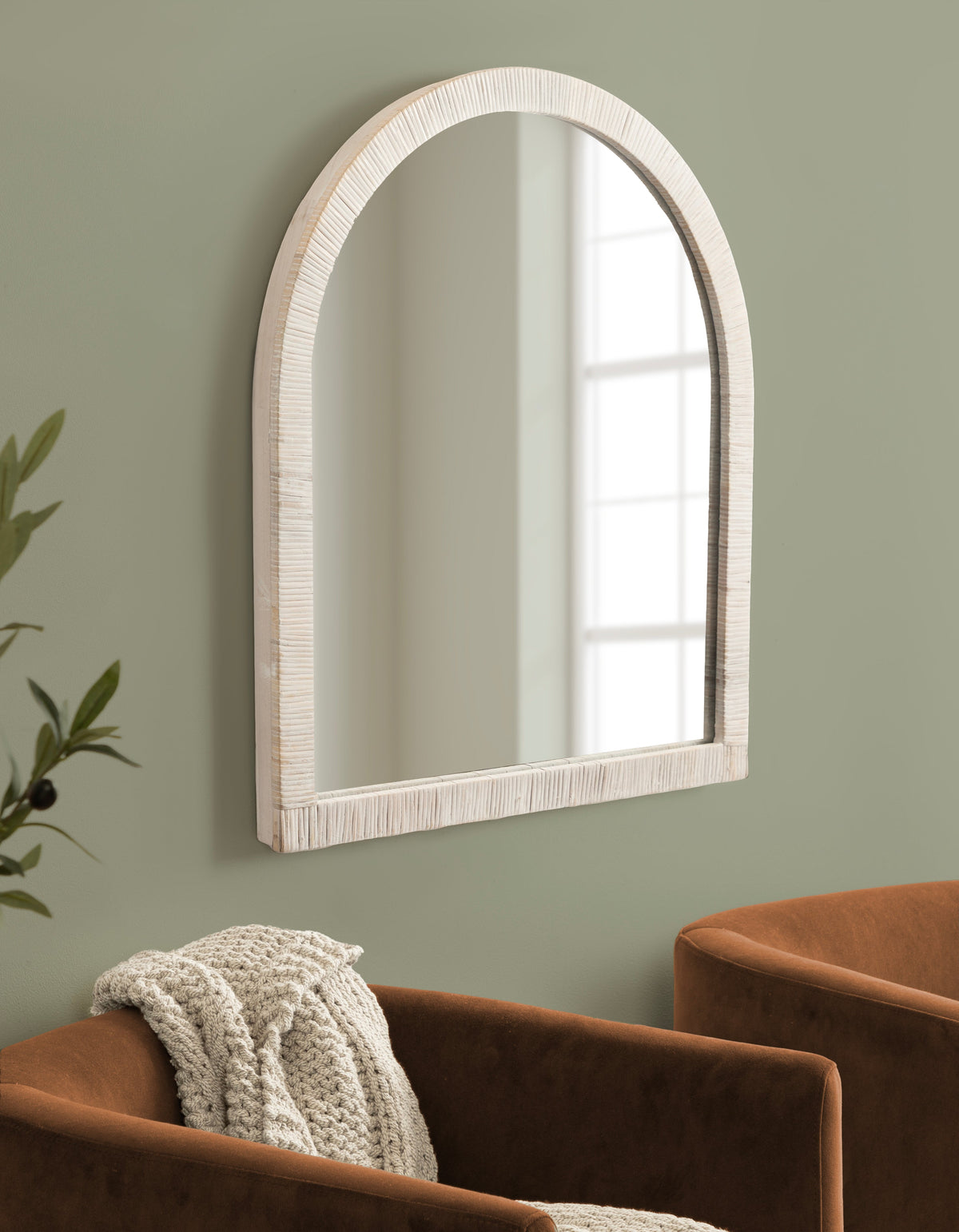 White rattan arched mirror styled on a sage-green wall